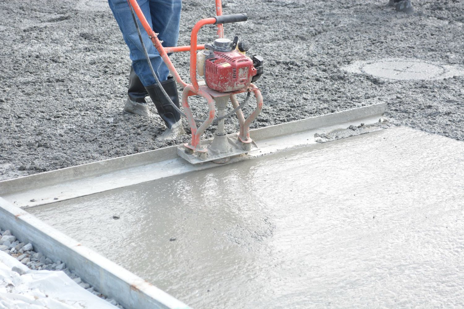Power screed leveling fresh concrete between forms